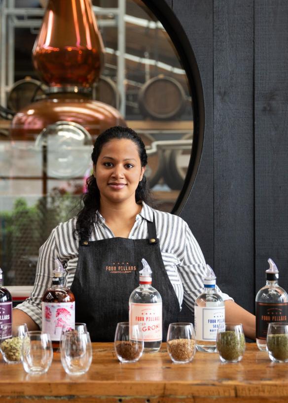 Une barmaid debout derrière une table sur laquelle sont posés des gins, des plantes aromatiques et des épices à la Four Pillars Gin Distillery, Yarra Valley, Victoria © Visit Victoria