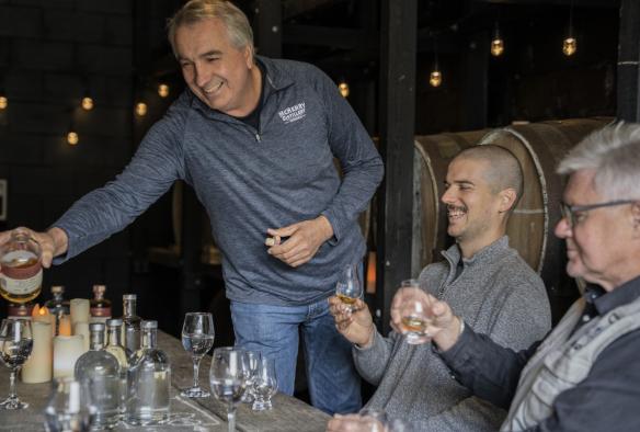 Un membre du personnel souriant et servant des spiritueux à base d'alcool aux invités assis à l'une des tables de la McHenry Distillery, Tasman Peninsula, Tasmanie © Tourism Australia