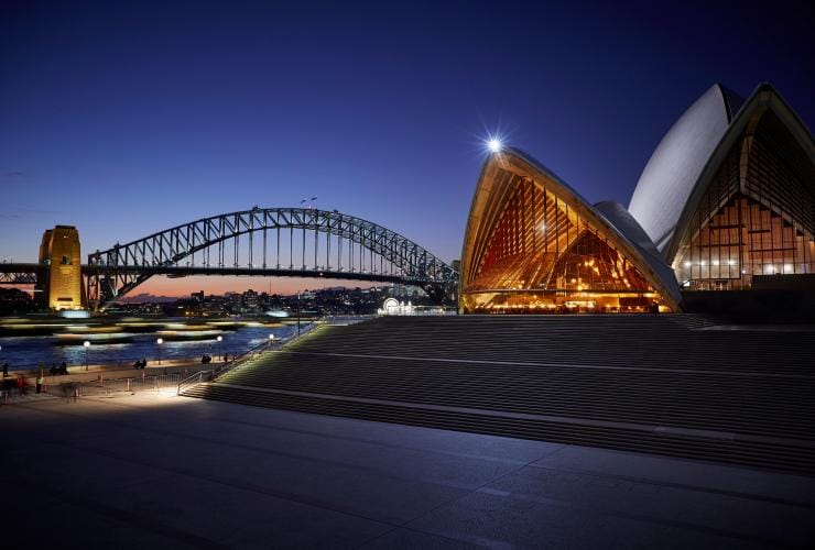 Une vue de l'intérieur d'un bâtiment triangulaire, baigné d'une lumière chaude, surplombant un port, restaurant Bennelong à l'Opéra de Sydney, Sydney, Nouvelle-Galles du Sud © Brett Stevens