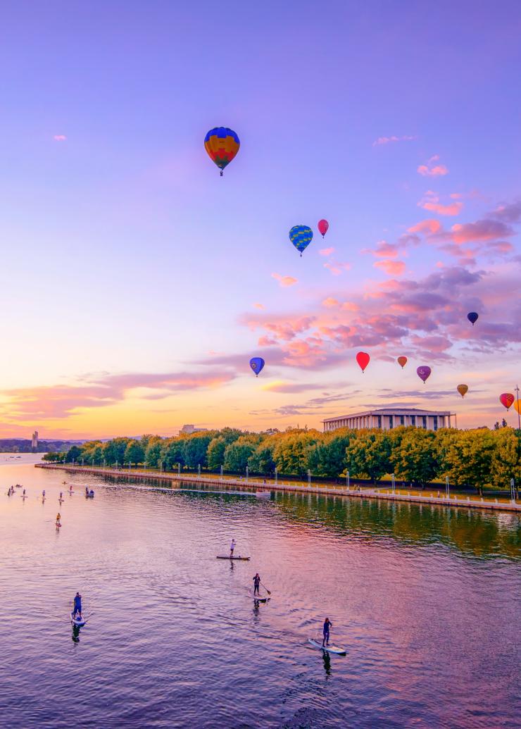 Des montgolfières flottant au-dessus d’un lac avec des personnes faisant du paddle pendant un coucher de soleil, Canberra Balloon Spectacular, Canberra, Territoire de la Capitale Australienne © Carol Elvin