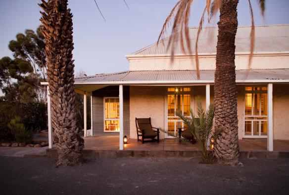 L'extérieur de la propriété du Arkaba Conservancy, avec des palmiers s'élevant devant un petit bâtiment blanc et des chaises posées sur le porche, Flinders Ranges, Australie du Sud © Arkaba Conservancy/Randy Larcombe