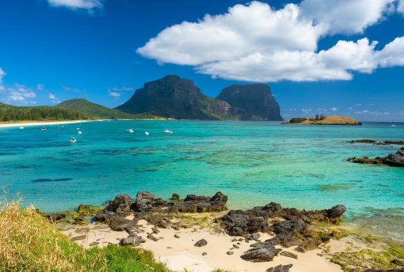 Vue de l'eau bleu vif de Lord Howe Island sur laquelle naviguent des bateaux, avec, en arrière-plan, les montagnes vertes de l'île, Nouvelle-Galles du Sud © Tourism Australia