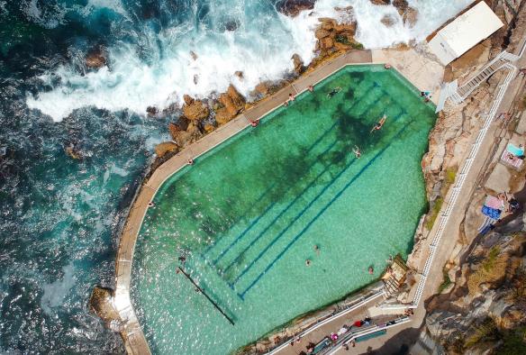 Vue aérienne de personnes nageant dans les Bronte Baths, avec les vagues de l'océan s'écrasant contre les parois à Bronte Beach, Sydney, Nouvelle-Galles du Sud © Ashlea Wheeler