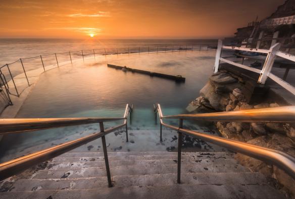 Des escaliers menant aux eaux claires et paisibles des Bronte Baths lors du coucher du soleil sur l'océan, Bronte Beach, Sydney, Nouvelle-Galles du Sud © Destination NSW