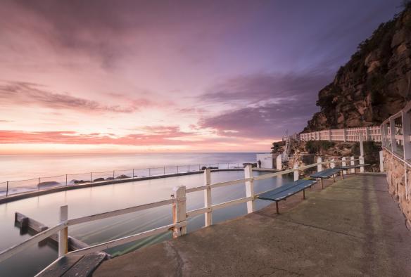 Des bancs publics nichés au-dessus des eaux paisibles des Bronte Baths, sous un ciel violet lors du coucher du soleil à Bronte Beach, Sydney, Nouvelle-Galles du Sud © Destination NSW