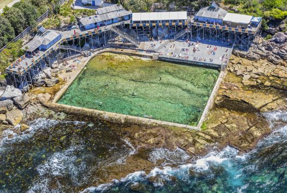 Vue aérienne de la piscine d'eau de mer des Wylie's Baths, dans laquelle des personnes nagent, entourée de rochers côtiers contre lesquels s'écrasent des vagues déferlantes, Coogee, Nouvelle-Galles du Sud © Destination NSW