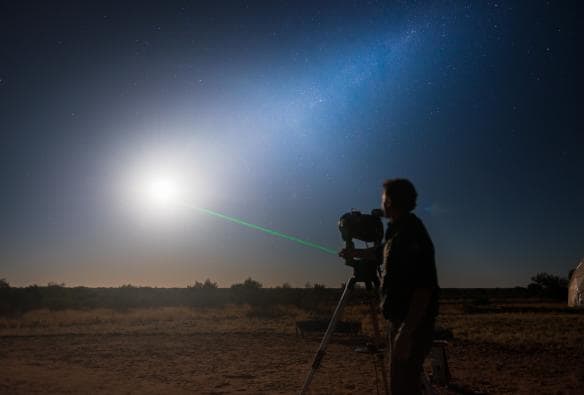 Un homme pointant un laser vers un ciel nocturne étoilé tout en regardant à travers un télescope à l'Earth Sanctuary, Alice Springs, Territoire du Nord © Tourism NT/Matt Glastonbury