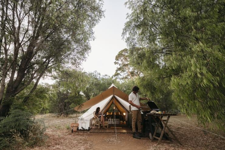 Une personne en train de cuisiner tandis qu’une autre est assise à côté d’une tente de glamping dans le bush, Walk Talk Taste, Margaret River, Australie Occidentale © Jarrad Seng