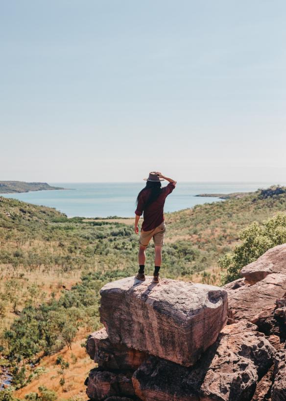 Une personne debout à l'extrémité d'une falaise rocheuse surplombant le bush, menant aux eaux bleues de l'océan, à Faraway Bay, le Kimberley, Australie Occidentale © Tourism Western Australia