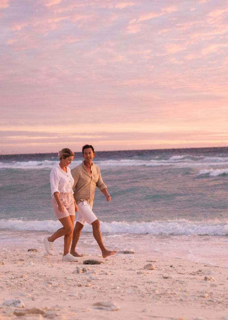 Homme et femme marchant sur la plage au coucher du soleil sur Lady Elliot Island Eco Resort, Grande Barrière de Corail, QLD © Tourism and Events Queensland