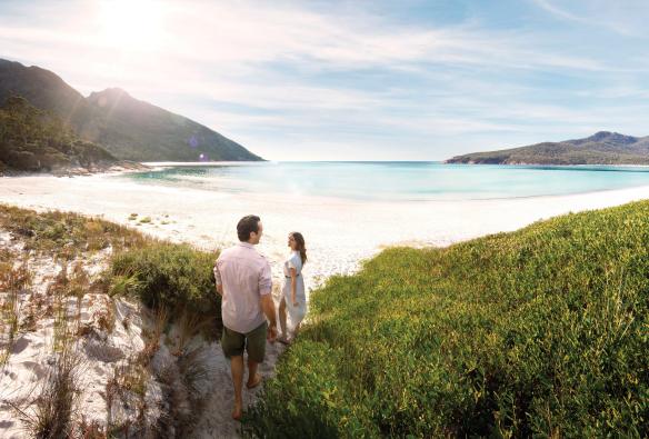 Couple marchant dans le bush et s'approchant de la plage de sable blanc aux eaux calmes et cristallines de Wineglass Bay, Freycinet National Park, Tasmanie © Myka Photography