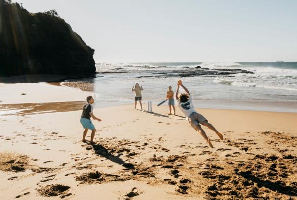 Empat orang teman bermain kriket di atas hamparan pasir di Coledale Beach, Thirroul, New South Wales © Destination NSW