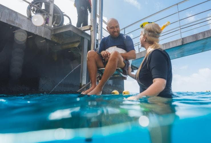 Seorang pria dengan mobilitas terbatas diturunkan ke samudra menggunakan lift di kapal Quicksilver Cruise, Great Barrier Reef, Queensland © Tourism and Events Queensland