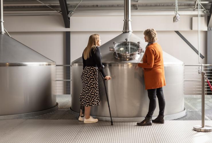Seorang wanita dengan alat bantu mobilitas berdiri bersama pemandu tur di Callington Mill Distillery, Oatlands, Tasmania © Dearna Bond