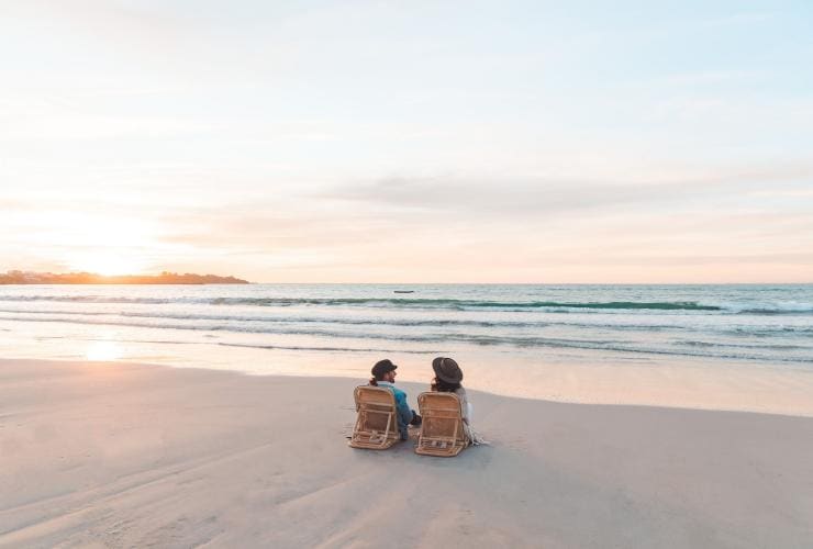 Pasangan duduk di pantai kosong saat matahari terbenam di Robe, Limestone Coast, South Australia © Mish and Kirk