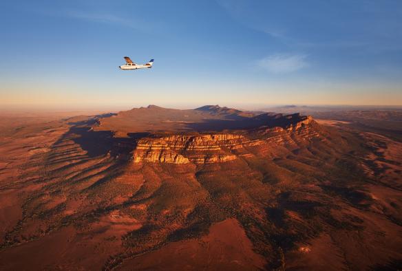 Pesawat kecil terbang di atas sebuah struktur pegunungan yang besar di pedalaman, Bush Pilots Scenic Flight, Wilpena Pound, Flinders Ranges National Park, South Australia © Adam Bruzzone