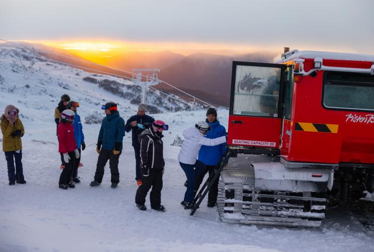 Sekelompok orang berdiri di atas gunung bersalju saat matahari terbit dengan warna keemasan yang cerah di Sunrise Sessions, Thredbo, New South Wales © Thredbo