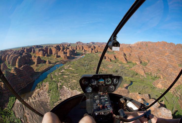 Pemandangan dari dalam helikopter ke arah serangkaian formasi bebatuan tinggi berbentuk kubah dengan garis-garis oranye dan cokelat bersama tur Heli Spirit, Bungle Bungles, Western Australia © Ben Knapinski
