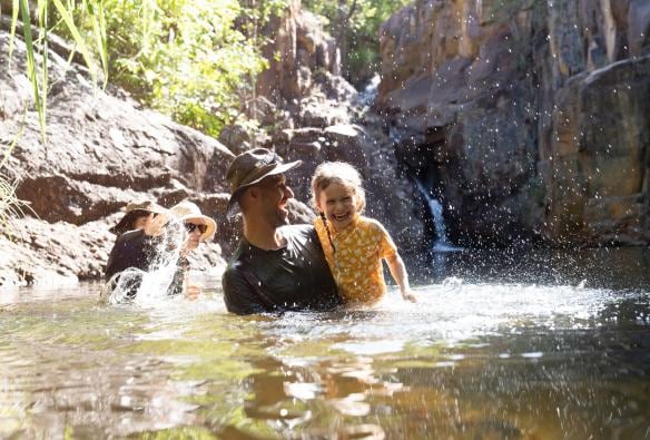 Ayah dan anak perempuannya tertawa sambil bermain air di kolam air alami dalam tur bersama Offroad Dreaming, Kakadu National Park, Northern Territory © Tourism Australia