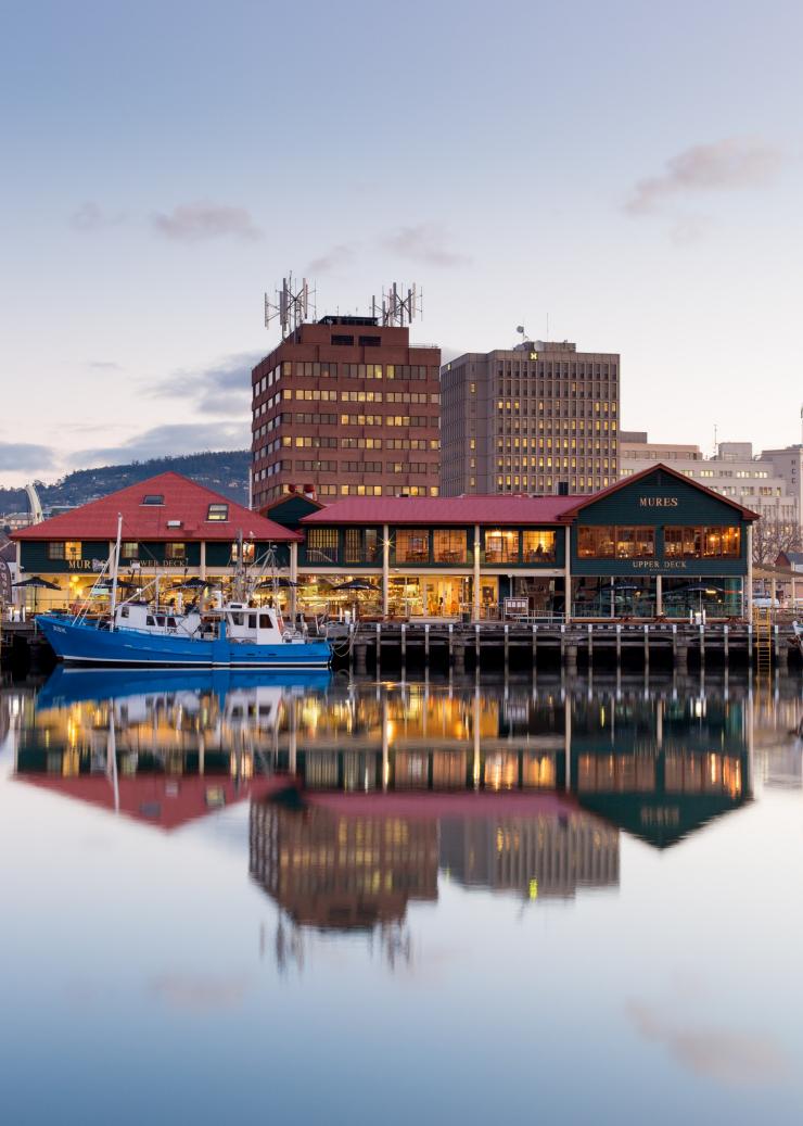 Restoran di tepi perairan yang tercermin pada permukaan laut di pelabuhan yang dipadati kapal, Mures Lower Deck, Hobart, Tasmania © Sam Shelley