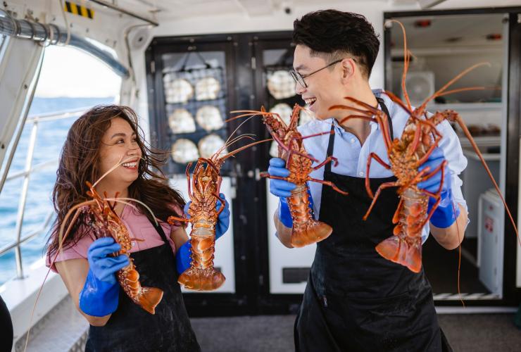 Dua orang memegang lobster yang baru ditangkap di atas perahu, Rottnest Cruises, Rottnest Island, Western Australia © Tourism Australia