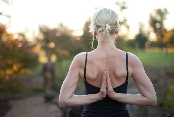 Seseorang berdiri di tengah padang semak sambil melakukan pose yoga dengan tangan di belakang punggung di Samadhi Retreat, Daylesford, Victoria © Samadhi Retreat/Marcus Struzina