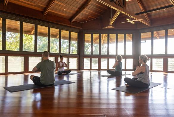 Tiga orang tamu dan seorang instruktur di dalam studio yoga sedang berlatih yoga di Gwinganna Lifestyle Retreat, Gold Coast, Queensland © Tourism Australia