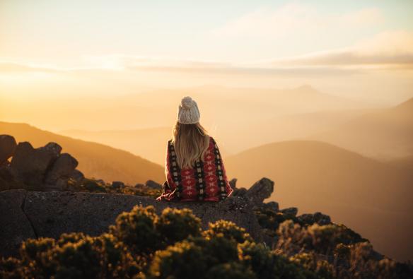 Seorang wanita duduk di puncak kunanyi/Mt Wellington yang menghadap ke arah Hobart yang diselimuti rona matahari terbit, Tasmania © Emilie Ristevski