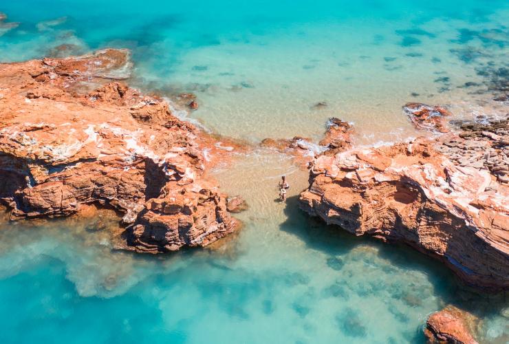 Pasangan berenang di perairan biru yang jernih di antara bebatuan merah di dekat Broome, Western Australia © Tourism Australia