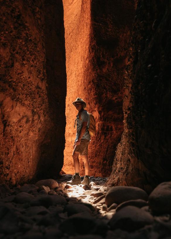 Seseorang berdiri di bawah bayangan antara dua dinding batu merah dengan terpaan sinar matahari di atas Echidna Chasm, Purnululu National Park, Western Australia © Tourism Western Australia