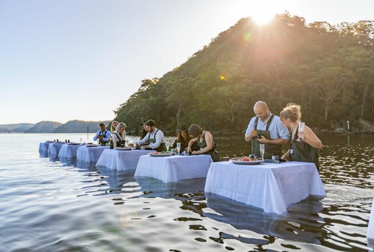 Pasangan berdiri di perairan sambil membuka oyster bersama Sydney Oyster Farm Tours, Mooney Mooney, New South Wales © Tourism Australia
