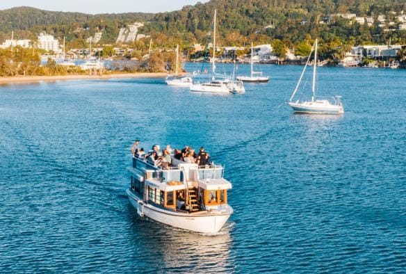 Vista aerea di una barca piena di persone che si allontana dalla costa coperta da vegetazione durante il Noosa Eat & Drink Festival, Noosa, Queensland © Tourism and Events Queensland