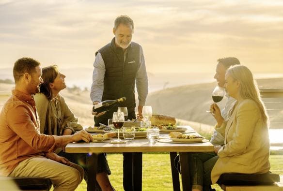 Un gruppo di persone mangia e beve al tramonto, Coast and Co, Carrickalinga, South Australia © Tourism Australia