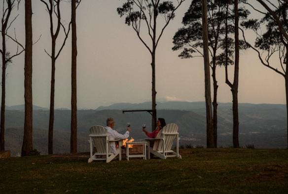 Un uomo e una donna seduti su sedie da giardino attorno a un braciere, Tamborine Mountain, Queensland © Reveling