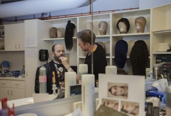 Un uomo applica del trucco sul viso di un attore in una sala dei costumi presso la Sydney Opera House, Sydney, New South Wales © Cultural Attractions of Australia 