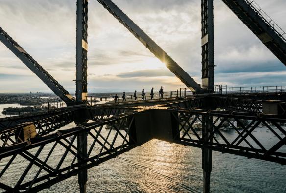 Un gruppo di persone che scala un ponte con arcate in acciaio sopra un porto durante il Burrawa Climb sul Sydney Harbour Bridge, Sydney, New South Wales © Destination NSW 
