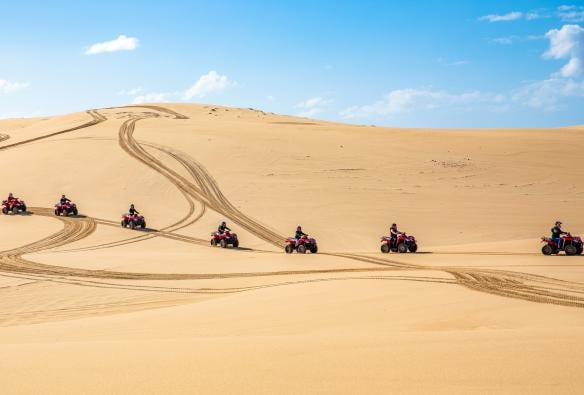 Una fila di persone a bordo di quad sulle dune di sabbia con Sand Dune Adventures a Stockton Beach, Port Stephens, New South Wales © Destination NSW