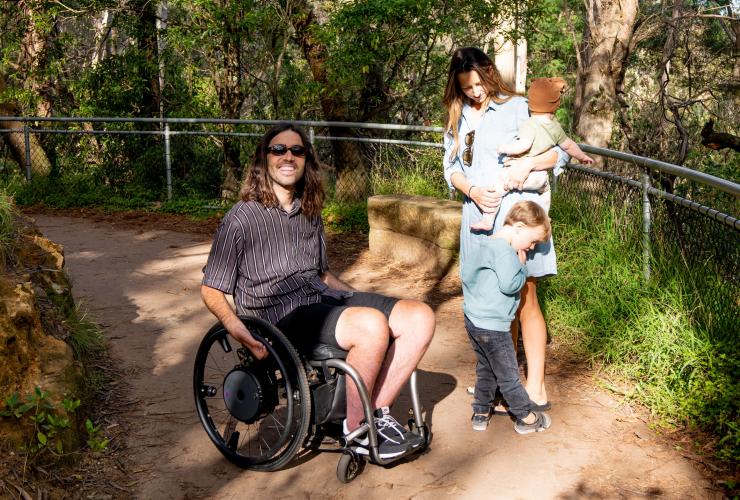 Uomo su una sedia a rotelle con la sua famiglia su un percorso nelle Blue Mountains, New South Wales © Tourism Australia