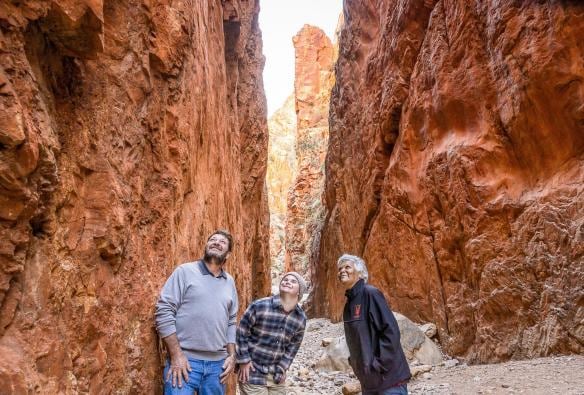 Uomo con una disabilità neurologica con una guida turistica e un altro uomo che guardano in alto a Standley Chasm, West MacDonnell Ranges, Northern Territory © Tourism NT/Helen Orr