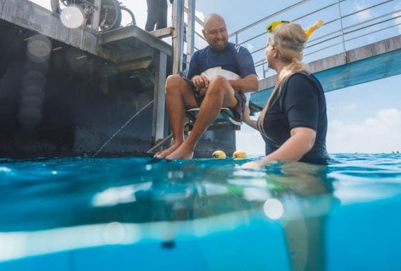 Uomo in sedia a rotelle che viene calato nell'oceano con un ascensore con Quicksilver Cruises, Grande Barriera Corallina, Queensland © Tourism and Events Queensland