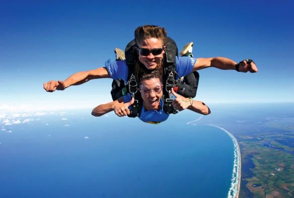 Due persone sorridenti che fanno skydiving in tandem sopra una costa coperta di vegetazione con Skydive Australia, Cairns, Queensland © Skydive Australia