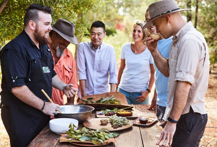 Un gruppo di persone riunite attorno a un tavolo con cibi del bush durante la Bush Food Experience, Yulara, Northern Territory © Voyages Indigenous Tourism