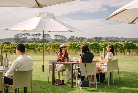 Un gruppo di persone mangia e sorseggia vino accanto a un vigneto, Pt. Leo Estate, Mornington Peninsula, Victoria © Visit Victoria