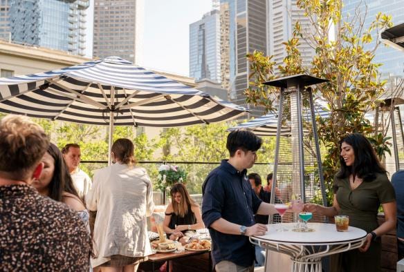Gruppi di persone che sorseggiano cocktail sotto gli ombrelloni in una giornata estiva al rooftop bar dell'Imperial Hotel, East End, Victoria © Jesse Hisco/Visit Victoria
