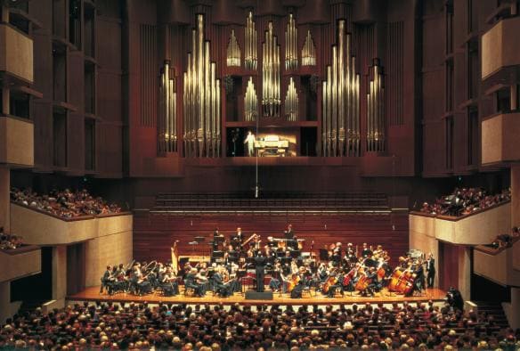 Orchestra su un palco in un teatro caratterizzato da pannelli in legno che si esibisce davanti a un folto pubblico al Queensland Performing Arts Centre, Brisbane, Queensland © Tourism and Events Queensland