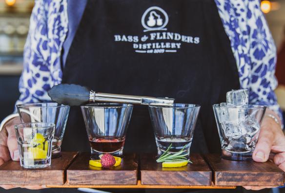 Barista che porta quattro diversi distillati su un vassoio con gli ingredienti davanti ai bicchieri alla Bass & Flinders Distillery, Mornington Peninsula, Victoria © Bass & Flinders
