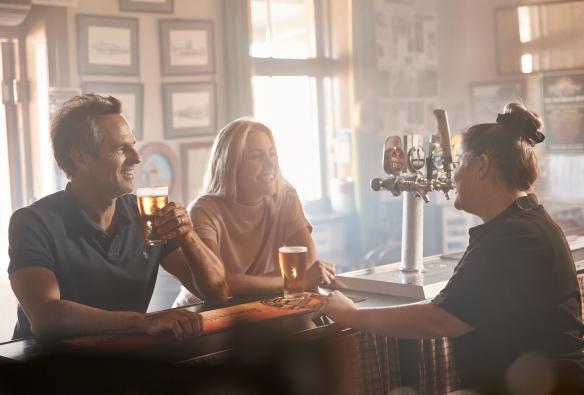Coppia che sorseggia una birra al bancone parlando con una barista al Silverton Hotel, Silverton, New South Wales © Destination NSW