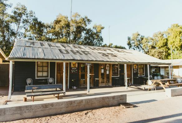 Un piccolo pub dell'outback con un tetto di stagno e tavoli fuori davanti alla vegetazione del bushland al Tilpa Hotel, Tilpa, New South Wales © Destination NSW