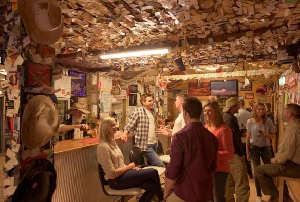 Un barista con cappello da cowboy che versa birra con una folla di persone nel pub al William Creek Hotel, Flinders Ranges & Outback, South Australia © South Australian Tourism Commission