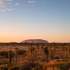 Un grande monolite di roccia rossa emerge dal paesaggio piatto dell'outback a Uluru, Uluru-Kata Tjuta National Park, Northern Territory © Tourism Australia